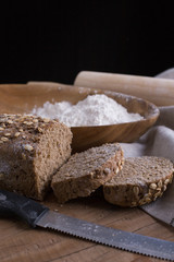 Whole grain wheat bread set on nice fabric brown background decorated with flour bowl and a bakery wooden roller.