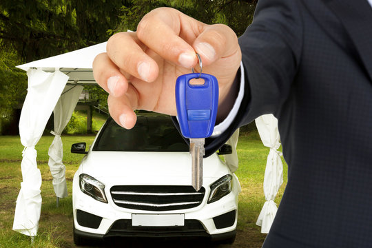 Man holding out a car key with a white luxury car parked behind him