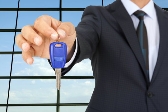 Man holding out a car key with business background	