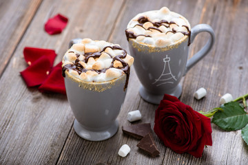 S'mores drink. Two mugs of hot chocolate with marshmallows on a wooden table. Cocoa. Rose petals. Valentine.