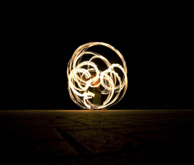 Man is spinning the poi with fire and making different shapes at night