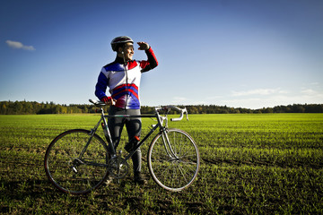 Fototapeta premium cyclist in the field next to the bicycle standing and looking forward for new horizonts on sunny day