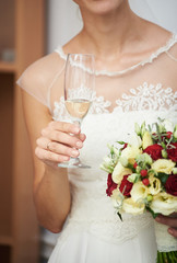 Bride is holding a wedding bouquet and a glass of champagne.