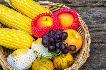 Group of organic fruits in fruit basket on wooden background.