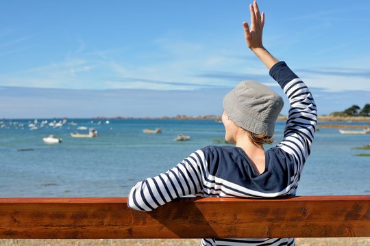 Une jeune femme habill&eacute;e d'un pull marin est assise sur un banc face &agrave; la mer
