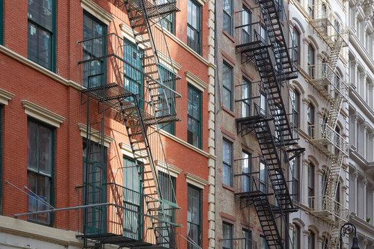 Typical building facades with fire escape stairs, sun beam in New York