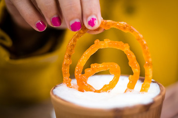 Jalebi being dipped in a earthenware milk cup by a lady in yellow. Jalebi is a very popular indian dish eaten alone or with milk