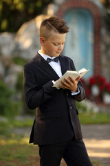 Śliczny model, chłopiec w garniturze z książeczką na tle kapliczki.
