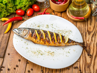 Fish cooked on fire on a white plate with lettuce leaves and parsley with lemon. restaurant supply