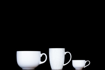 Obraz premium Three white cups with different shapes. Mugs standing in row in black background