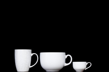 White cups in black backgrounds. Three mugs of different shapes standing in black background