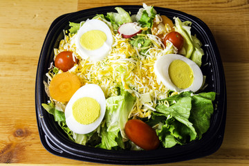 fresh garden salad of lettuce tomato carrot radish cheese and egg on wood background