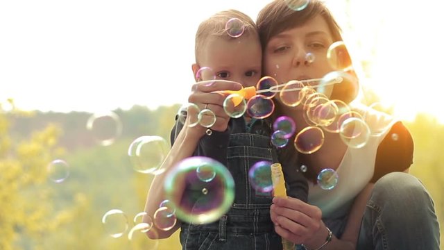 Young mother and her two years old baby boy playing in park with soap bubbles