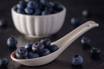 Fresh picked blueberry in spoon and bowl on black background, selective focus