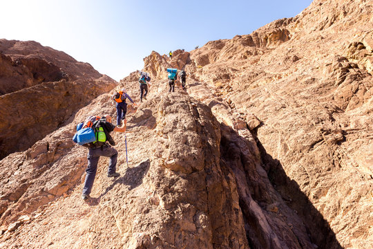 Group backpackers ascending climbing desert mountain trail lifestyle.