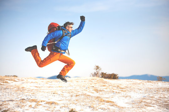 A man with a backpack jumps on the background mountain.