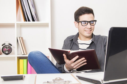 Young Man In House Or Office With The Book Or Calendar And Notebook Computer