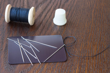 Spool of black thread, a needle and white sewing thimble  on the