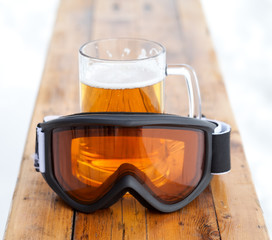 Ski goggles and glass mug with fresh cold beer