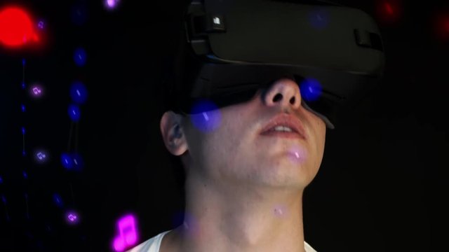 Smiling young man wearing VR Headset experiencing virtual reality. Musical notes and 3d objects flying around head.