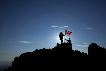 Two soldiers raise the Canadian flag on a mountain top