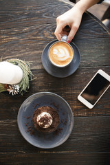 Dessert and cappuccino on a table, female hand keep cup