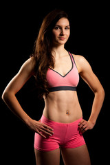 Fototapeta na wymiar Cute fit woman with pink sport dress poses over black background