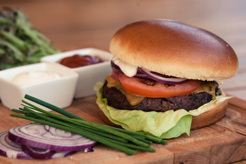beef burger on a wooden table with herbs, onions and tomatoes