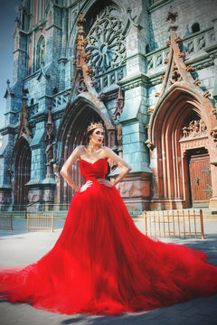 Beautiful girl in long red dress and in royal crown nearly catholic cathedral