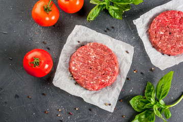 Fresh raw home-made minced beef steak burger with spices, basil and tomatoes on a cutting board on a stone table, copy space, top view