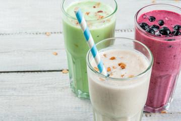 Refreshing milkshakes or smoothies: White (banana), green (apple and kiwi) and berries. On a white wooden table, copy space