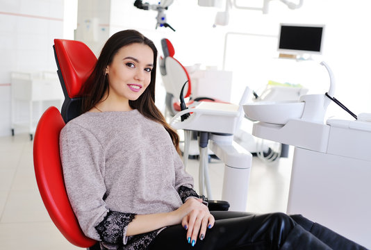 attractive girl in red dental chair at the reception of dentists. Dentistry, teeth whitening, dental fillings, smile, tooth decay.