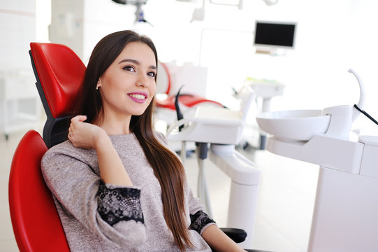 attractive girl in red dental chair at the reception of dentists. Dentistry, teeth whitening, dental fillings, smile, tooth decay.