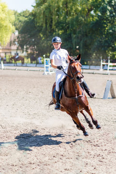 Young rider girl on bay horse on equestrian competition at hot summer day