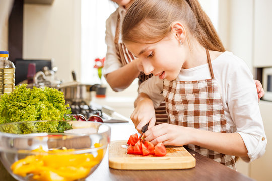 Young teenage girl cooking together with her family in the kitchen. Cute girl chopping tomatoes for salad
