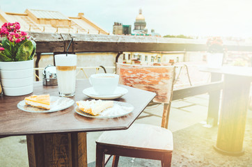 Top view two coffee cups with piece of white new york cheesecake and orange cake on brown wooden table, outdoor street cafe in Saint-Petersburg, Russia. Latte Glass americano. Copy space