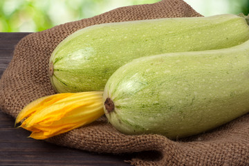 two courgettes with a flower on sackcloth wooden background