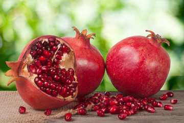 two whole pomegranate and half on the old wooden board with blurred garden background
