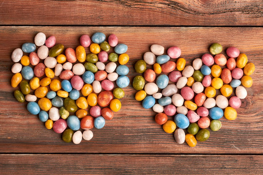 Colorful candy hearts on wood. Heart-shaped candy pebble piles. Confectionery as art.