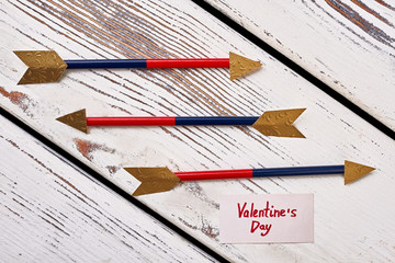 Arrows and Valentine's Day card. Greeting paper on wooden plank. Cupid as symbol of love.