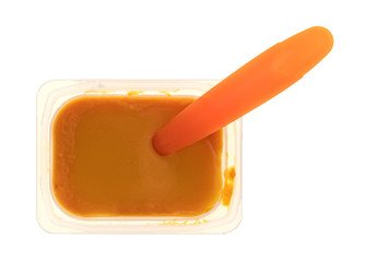Baby food in a plastic container with a spoon inserted into the food isolated on a white background.