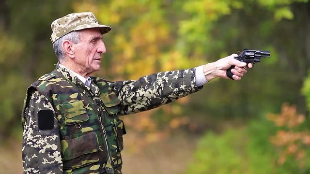 Man with black gun. Senior man in military uniform shoots a revolver. Retired officer at shooting range. Senior man in military uniform shoots a pistol in forest