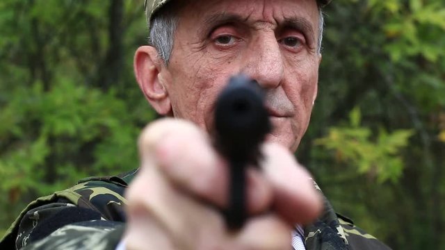 Man with black gun looks at the camera. Retired officer in military uniform at shooting range. Man holds in hands black revolver