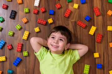 Little caucasian child playing with lots of colorful plastic blocks indoor. Kid boy wearing  shirt...