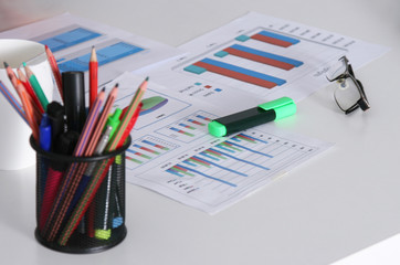 Closeup of white desktop with laptop, glasses, coffee cup, notepads and other items on blurry city background