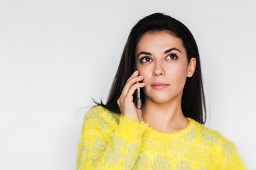 Close up portrait of serious young beautiful woman using smart phone over light grey background. Pretty brunette woman using device, talking on mobile phone and look up. Technology theme.