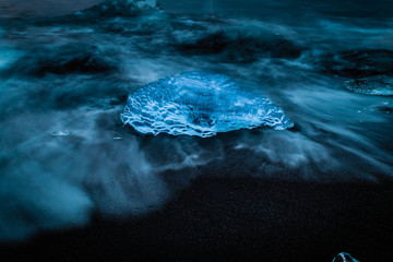 Iceland ice shard block crystal clear on black beach with water at Jokulsarlon glacier lagoon...