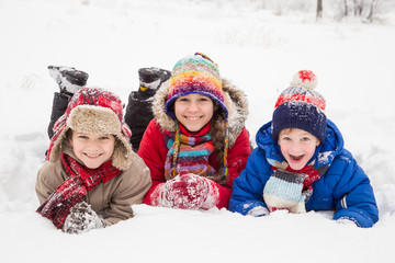 Three kids lying down together on winter snow