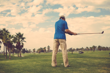 Man holding playing vintage wooden golf club on grass field outdoors background. Back view of active male
