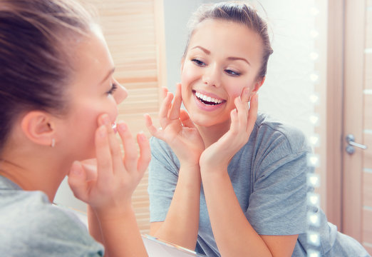 Skincare. Young beautiful teenage girl touching her face before the mirror, enjoying her clean skin